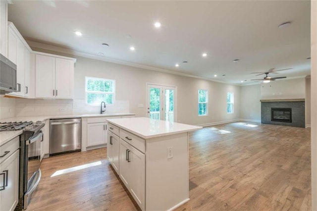 kitchen with appliances with stainless steel finishes, crown molding, ceiling fan, a center island, and decorative backsplash