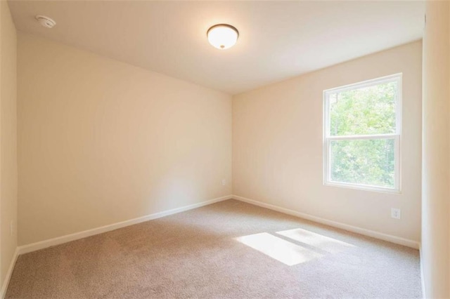 carpeted empty room featuring baseboards and a smoke detector