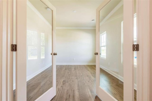hall with wood finished floors, ornamental molding, baseboards, and french doors