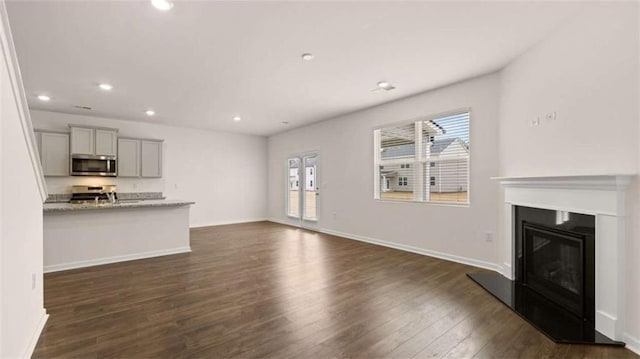 unfurnished living room with a glass covered fireplace, dark wood-type flooring, recessed lighting, and baseboards