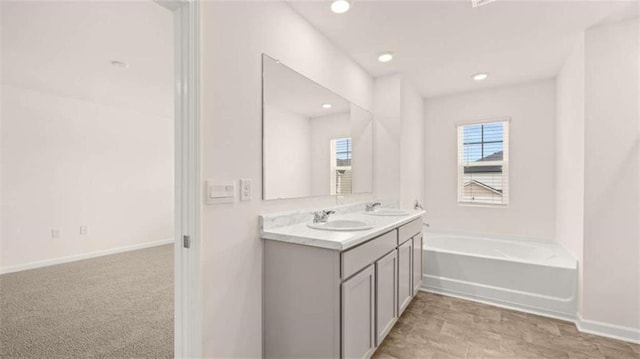 bathroom with a garden tub, double vanity, baseboards, and a sink