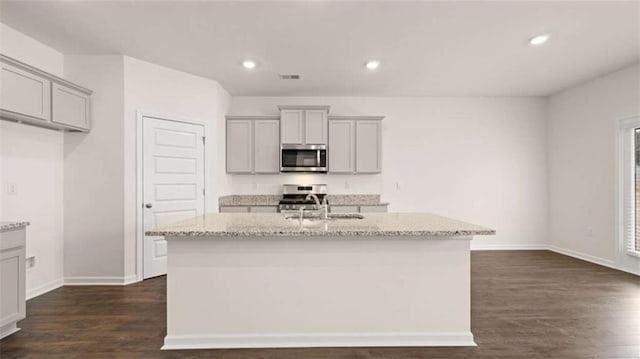 kitchen featuring a kitchen island with sink, gray cabinets, light stone counters, dark wood finished floors, and stainless steel appliances
