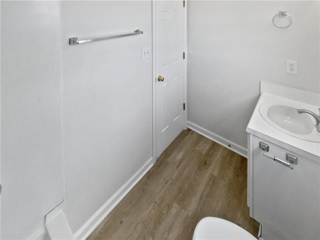 bathroom with toilet, vanity, baseboards, and wood finished floors