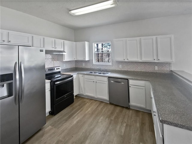 kitchen with light wood finished floors, under cabinet range hood, appliances with stainless steel finishes, white cabinets, and a sink