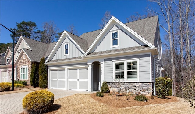 view of front facade with stone siding, board and batten siding, driveway, and roof with shingles