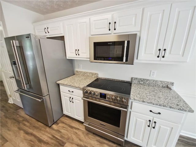 kitchen with stainless steel appliances, dark wood finished floors, white cabinetry, and light stone counters