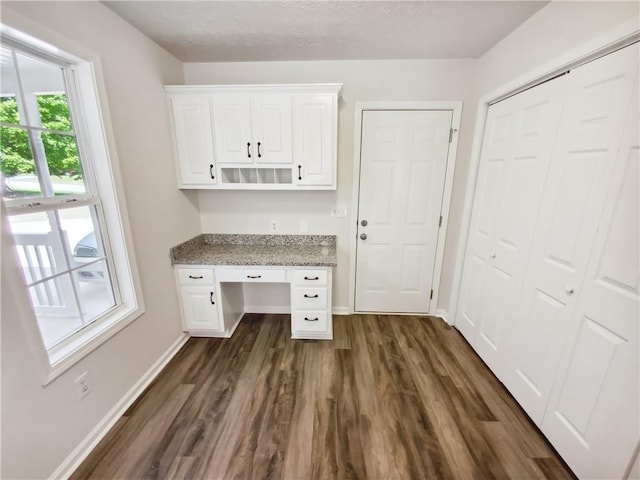 unfurnished office with dark wood-style flooring, baseboards, and built in study area