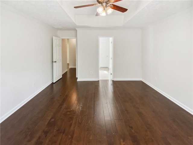unfurnished room featuring a tray ceiling, dark wood-type flooring, ceiling fan, and baseboards