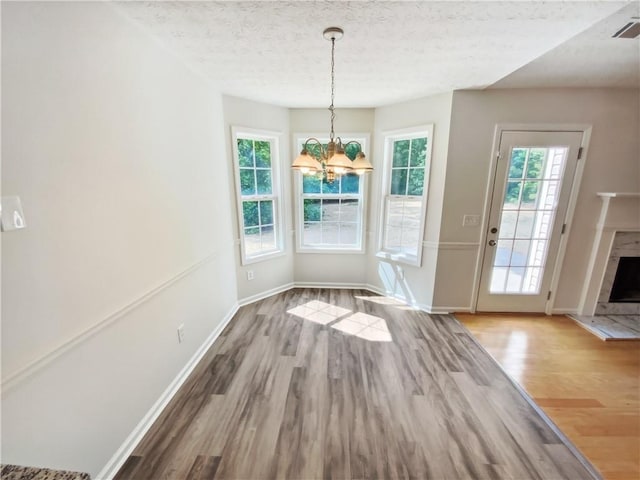 unfurnished dining area featuring wood finished floors, healthy amount of natural light, a chandelier, and a textured ceiling