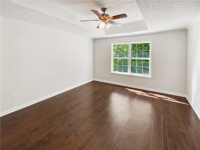empty room featuring a tray ceiling, dark wood-style floors, ceiling fan, baseboards, and a textured ceiling