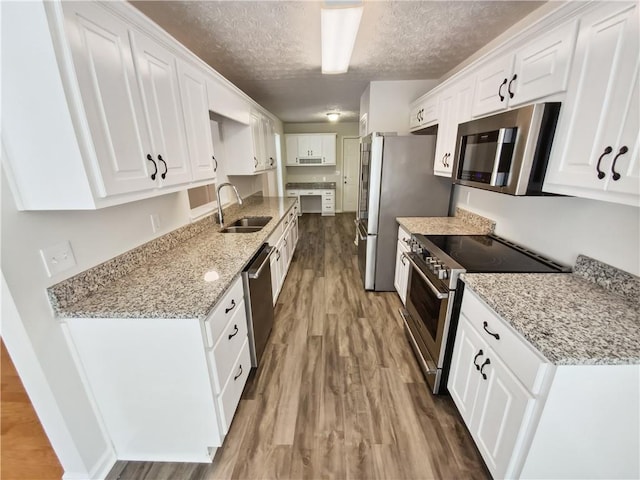 kitchen with stainless steel appliances, a sink, wood finished floors, white cabinets, and a textured ceiling