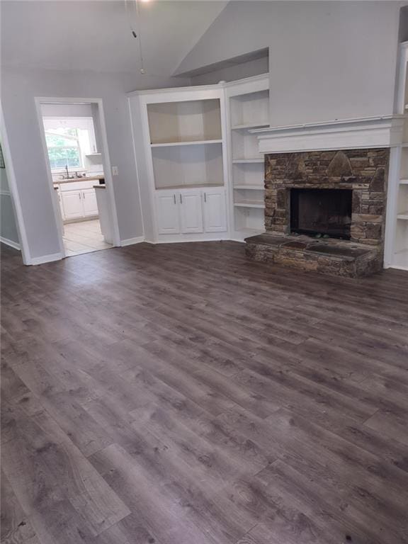 unfurnished living room with built in features, a stone fireplace, dark wood-type flooring, and lofted ceiling