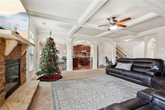 living area featuring arched walkways, decorative columns, visible vents, a stone fireplace, and coffered ceiling