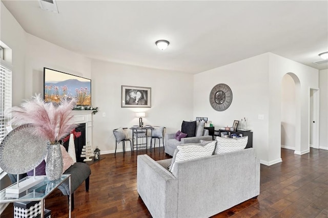 living area featuring baseboards, visible vents, arched walkways, a fireplace with raised hearth, and dark wood-type flooring