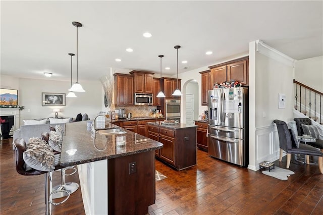 kitchen with arched walkways, a peninsula, appliances with stainless steel finishes, and hanging light fixtures