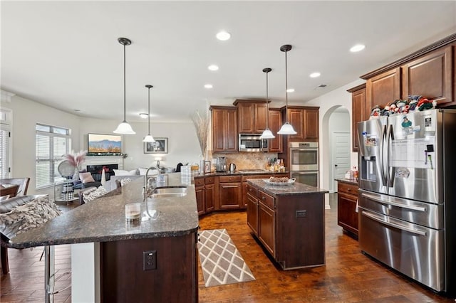 kitchen with appliances with stainless steel finishes, open floor plan, decorative light fixtures, a kitchen island with sink, and a sink