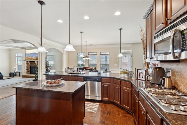 kitchen with pendant lighting, stainless steel appliances, open floor plan, a sink, and a stone fireplace