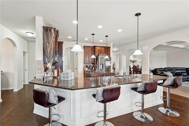 kitchen featuring a breakfast bar, arched walkways, pendant lighting, and dark stone counters