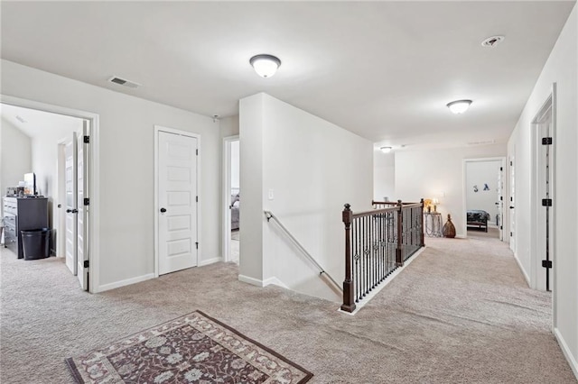 hall featuring light carpet, visible vents, an upstairs landing, and baseboards