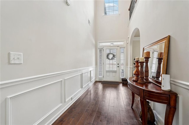 foyer featuring plenty of natural light, arched walkways, dark wood finished floors, and a decorative wall