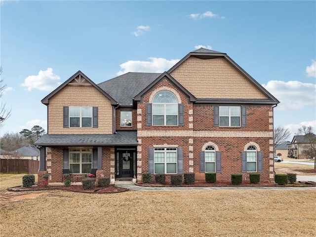 craftsman-style house with a front lawn, a shingled roof, and brick siding