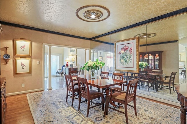 dining area featuring a textured ceiling, baseboards, decorative columns, and light wood-style floors