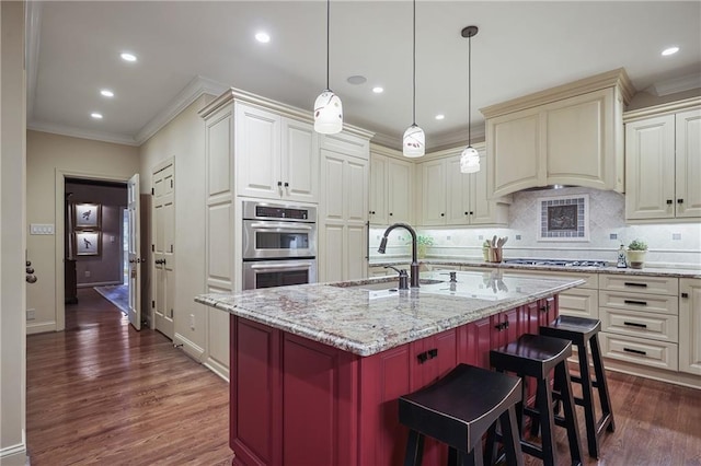 kitchen featuring crown molding, stainless steel appliances, a sink, light stone countertops, and a kitchen bar