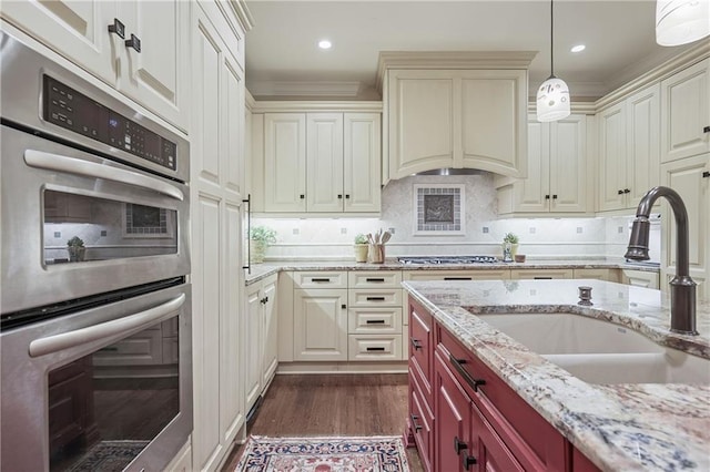 kitchen with decorative backsplash, dark wood-type flooring, hanging light fixtures, stainless steel appliances, and a sink