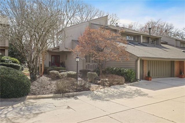 mid-century modern home featuring concrete driveway, brick siding, and roof with shingles