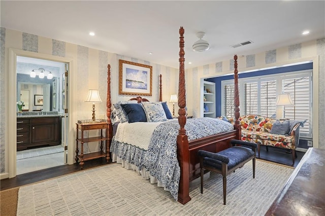 bedroom with light wood-style floors, ensuite bath, visible vents, and wallpapered walls