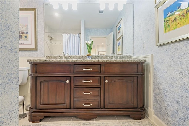 full bathroom with a sink, visible vents, tiled shower, double vanity, and wallpapered walls