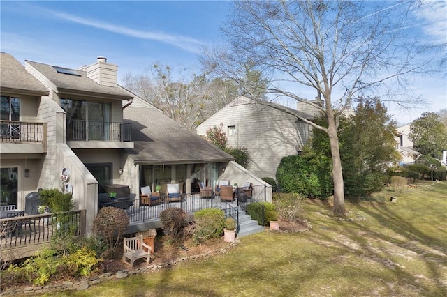 rear view of house featuring a shingled roof, a lawn, a chimney, and a balcony