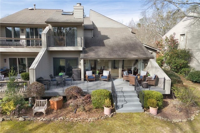 back of property featuring a shingled roof, a chimney, a balcony, and an outdoor hangout area