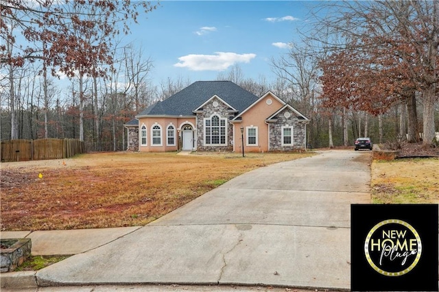 view of front facade with stone siding, fence, concrete driveway, and a front yard