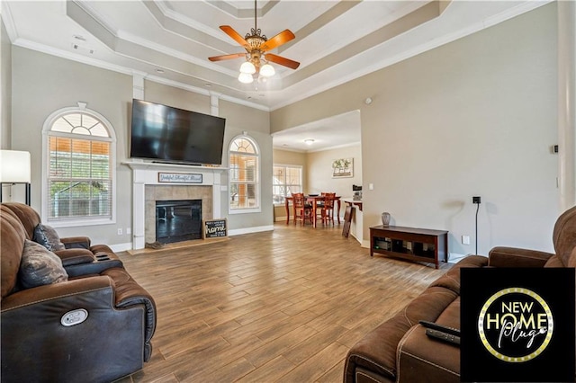 living room featuring a tray ceiling, crown molding, baseboards, and wood finished floors