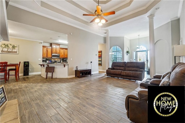 living area featuring a tray ceiling, decorative columns, ornamental molding, wood finished floors, and baseboards