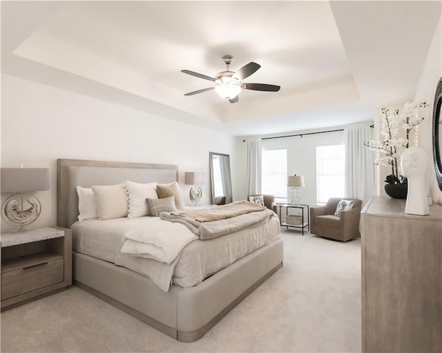 bedroom featuring a tray ceiling, light colored carpet, and ceiling fan