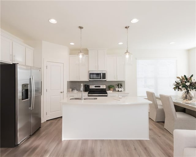 kitchen with a center island with sink, appliances with stainless steel finishes, pendant lighting, and white cabinets