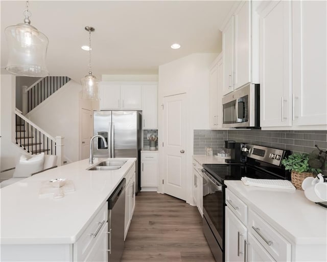 kitchen with stainless steel appliances, white cabinetry, an island with sink, and decorative light fixtures