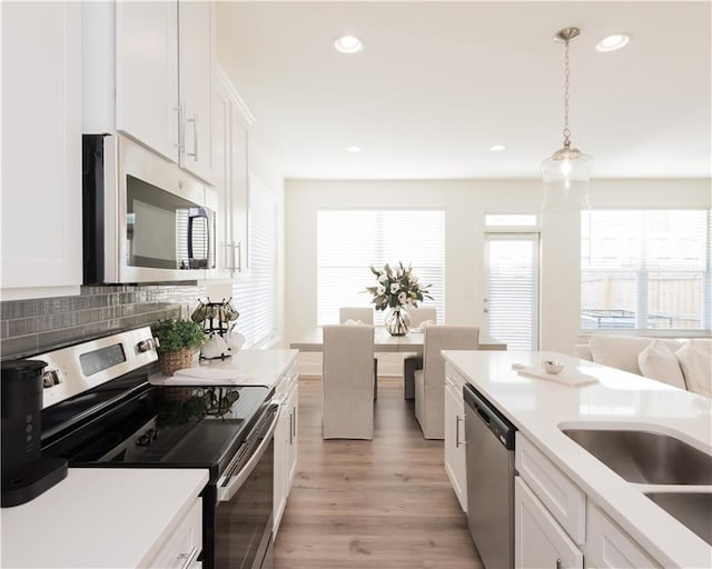 kitchen with appliances with stainless steel finishes, tasteful backsplash, white cabinets, hanging light fixtures, and plenty of natural light