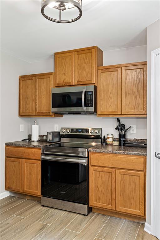 5706 Forest Pl, Acworth, GA 30102 - kitchen featuring appliances with stainless steel finishes, dark countertops, light wood-style floors, and brown cabinetry