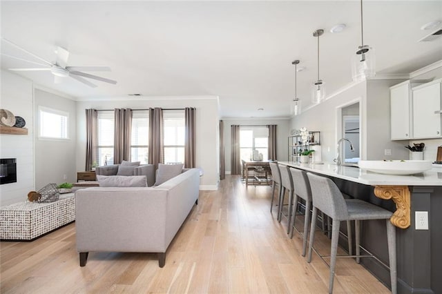 living room featuring a large fireplace, sink, ornamental molding, ceiling fan, and light hardwood / wood-style floors