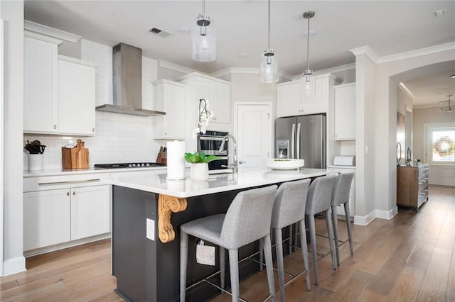 kitchen with wall chimney exhaust hood, appliances with stainless steel finishes, a center island with sink, and white cabinets