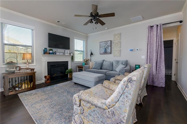 living area featuring a glass covered fireplace, ornamental molding, dark wood finished floors, and visible vents