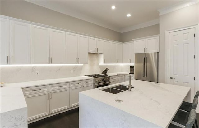 kitchen featuring sink, white cabinetry, premium appliances, an island with sink, and a kitchen bar