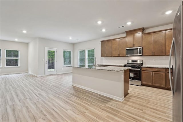 kitchen with light stone countertops, appliances with stainless steel finishes, light wood-type flooring, sink, and a center island with sink