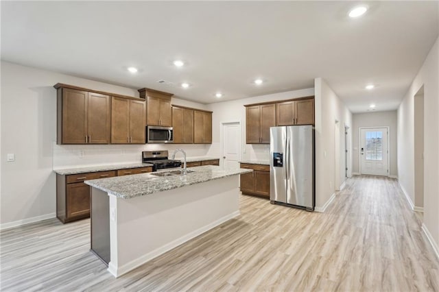 kitchen featuring a kitchen island with sink, sink, light hardwood / wood-style flooring, light stone countertops, and stainless steel appliances