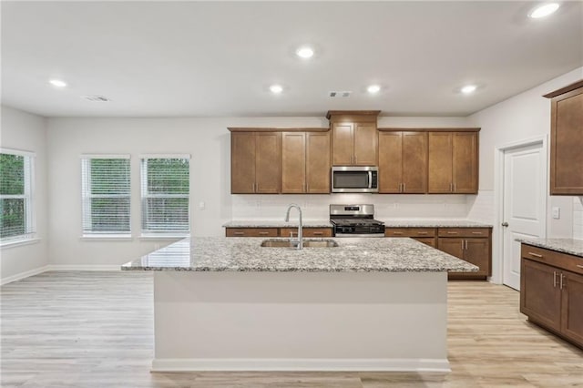 kitchen featuring sink, light stone counters, an island with sink, light hardwood / wood-style floors, and appliances with stainless steel finishes