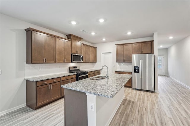 kitchen featuring light stone countertops, stainless steel appliances, sink, a center island with sink, and light hardwood / wood-style floors