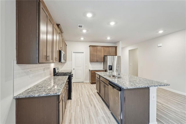 kitchen featuring light stone countertops, decorative backsplash, a kitchen island with sink, and stainless steel appliances